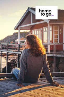 Frau sitzt entspannt vor einem Ferienhaus am See in Skandinavien symbolisiert Angebote von HomeToGo